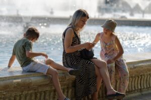 Woman on smartphone beside river with children